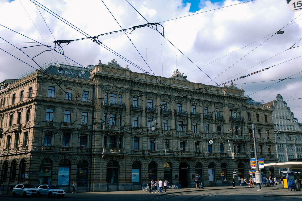An ornate historic building in a city centre with visible tram lines and street activity.