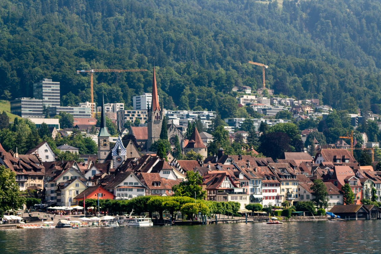A lakeside Swiss old town with a clock tower and mountains behind.
