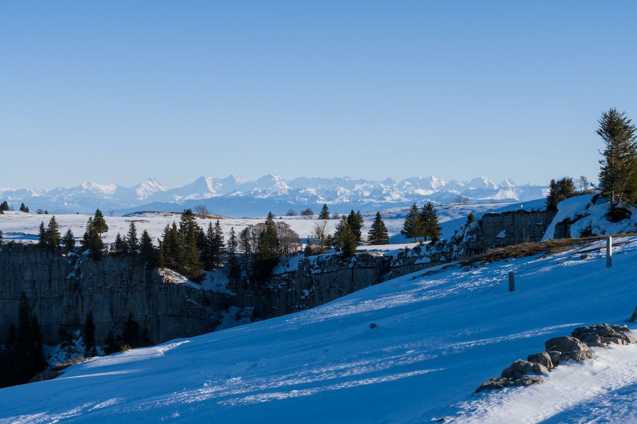 A snow-covered rocky cliff with distant mountains.