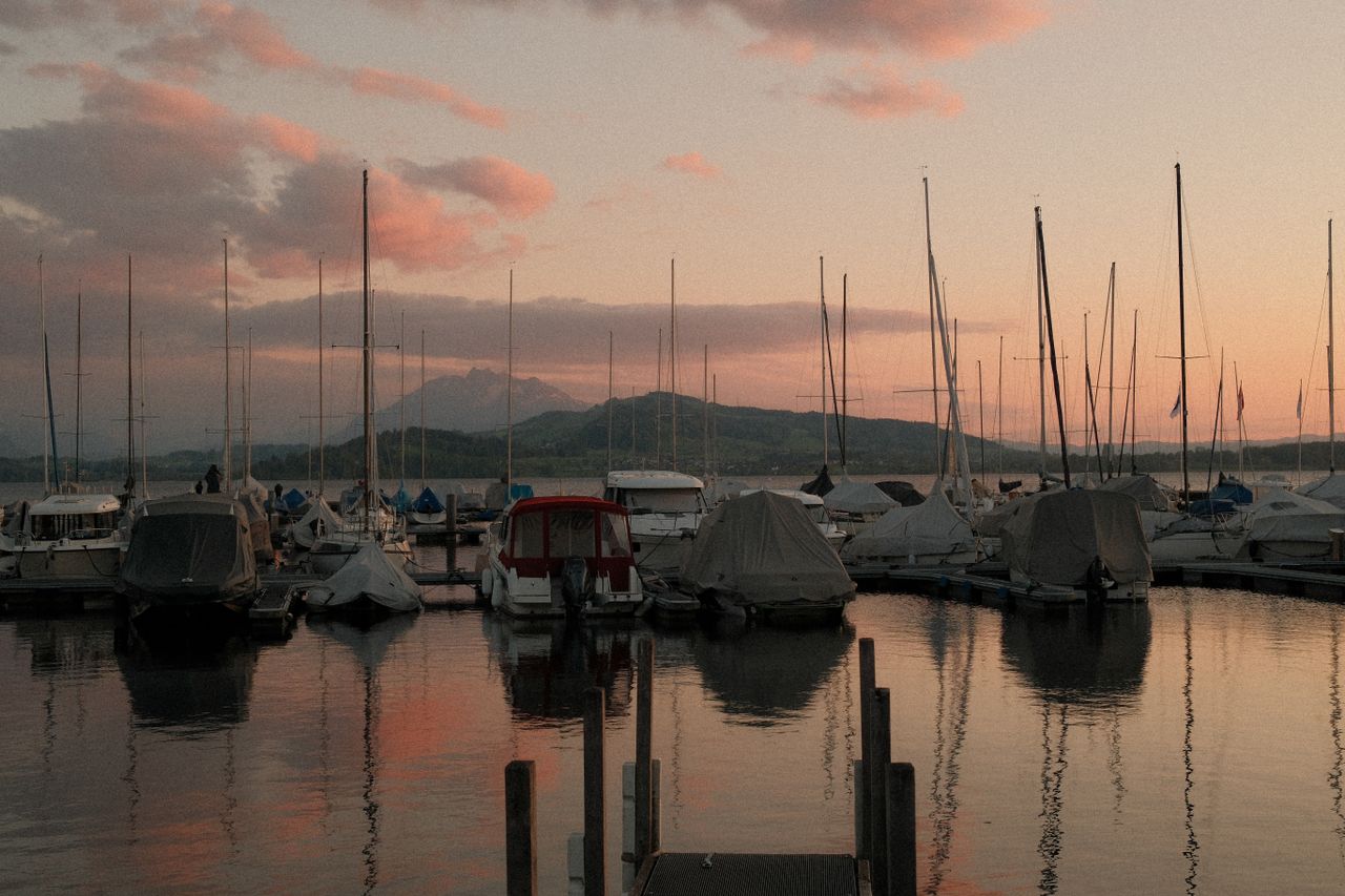 Sailboats moored in a marina at sunset with mountains behind.