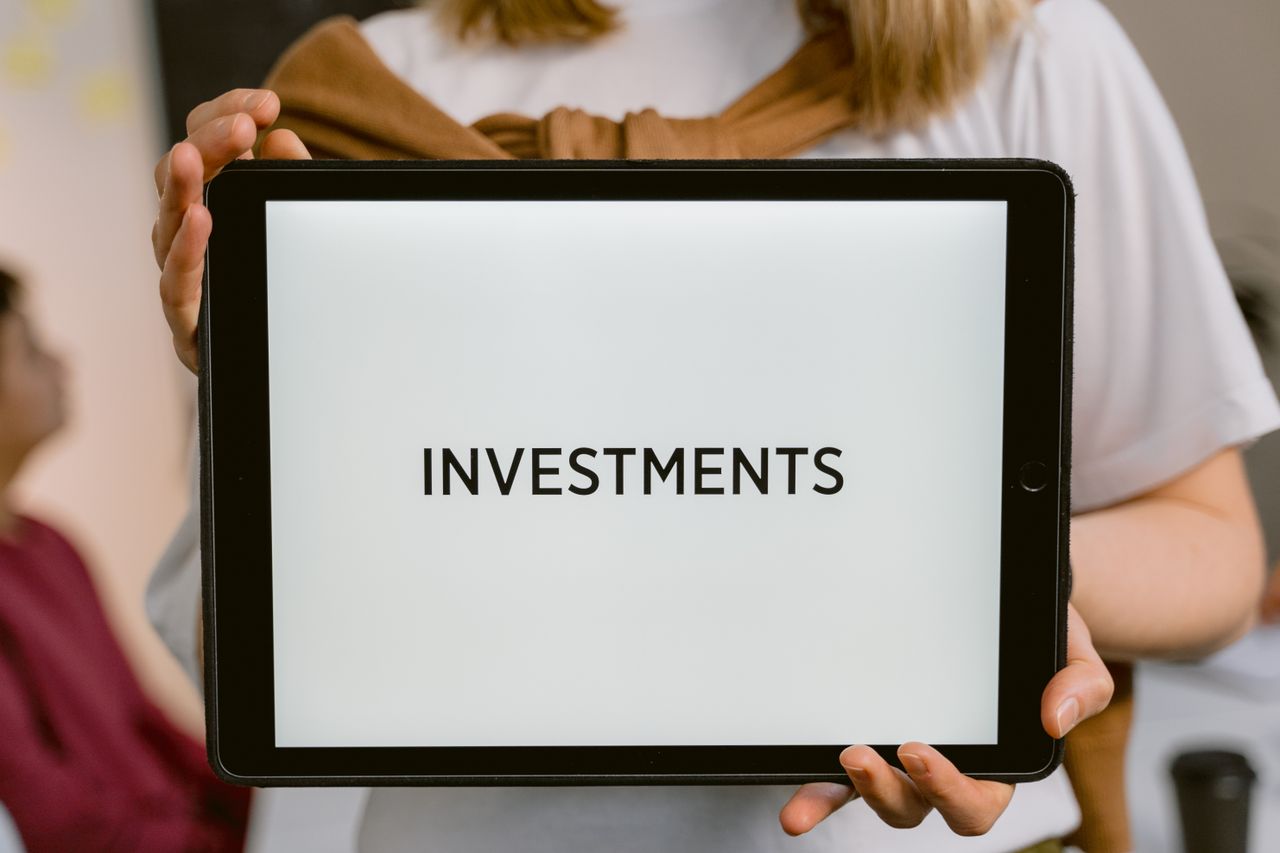 A hand holding a tablet that displays the word 'Investments'.