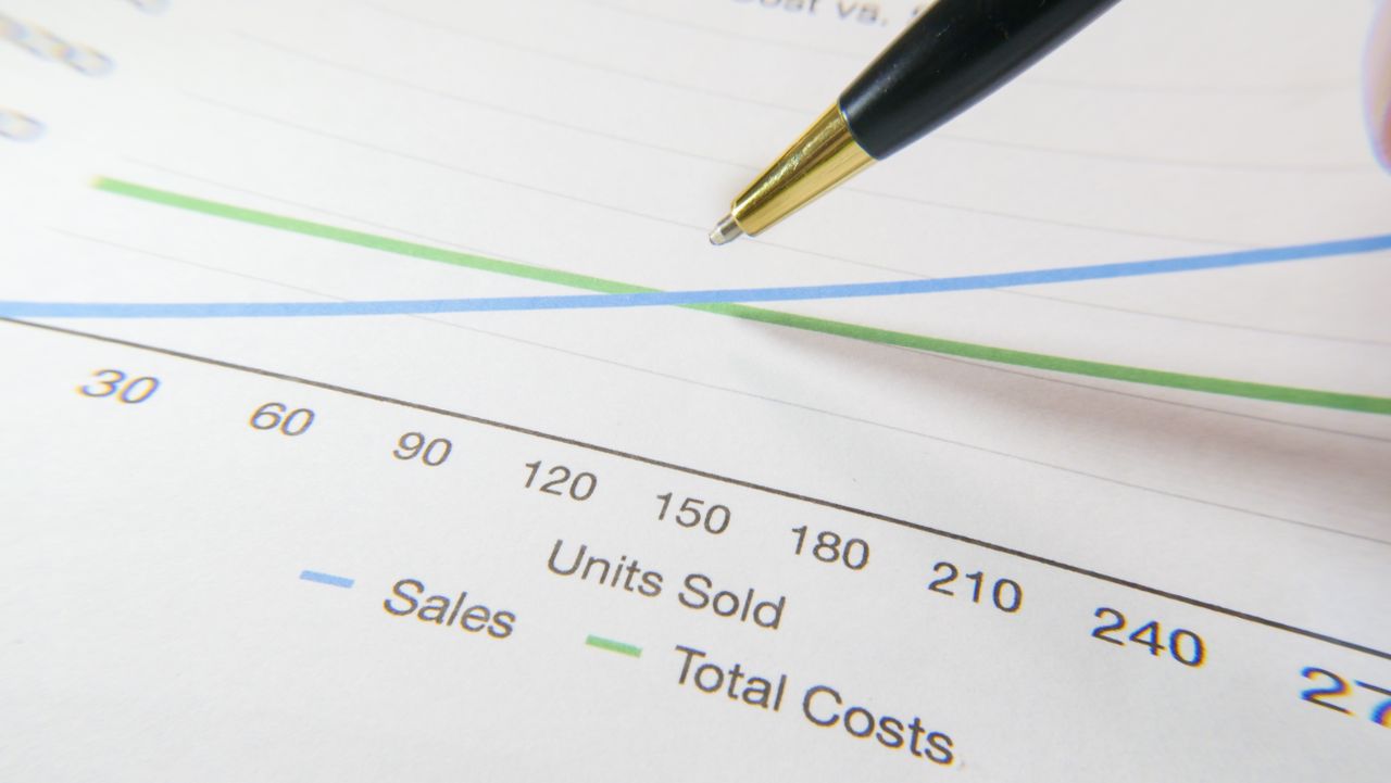 A pen resting on a printed chart that plots sales against total costs.