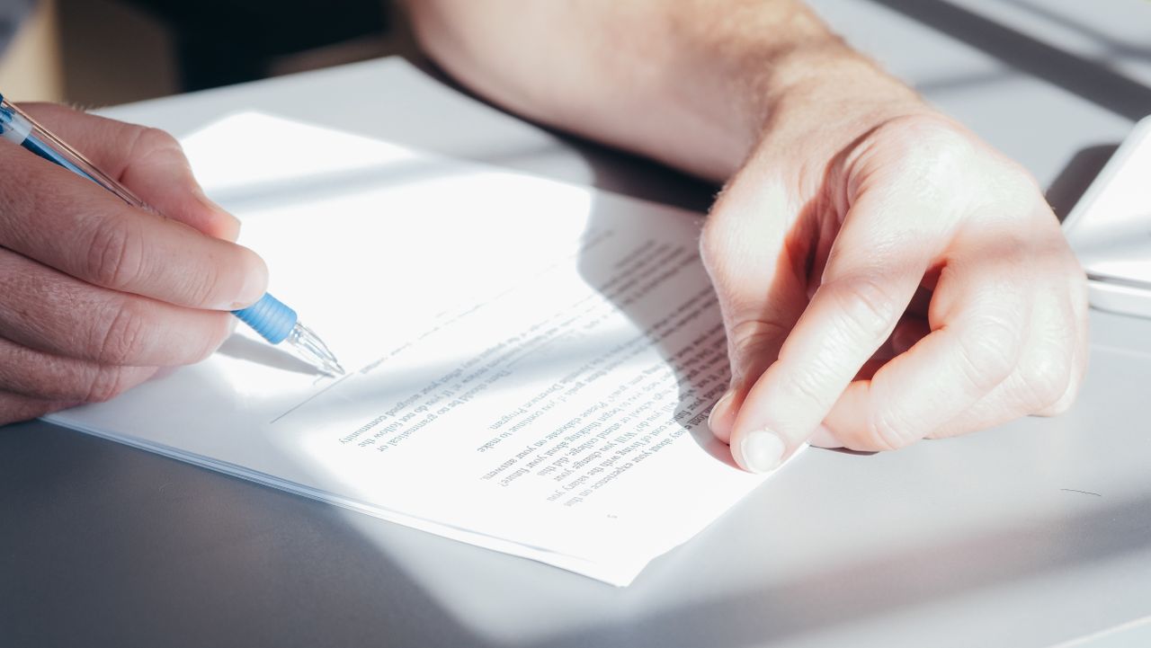 Close-up of hands signing a printed document with a blue pen.