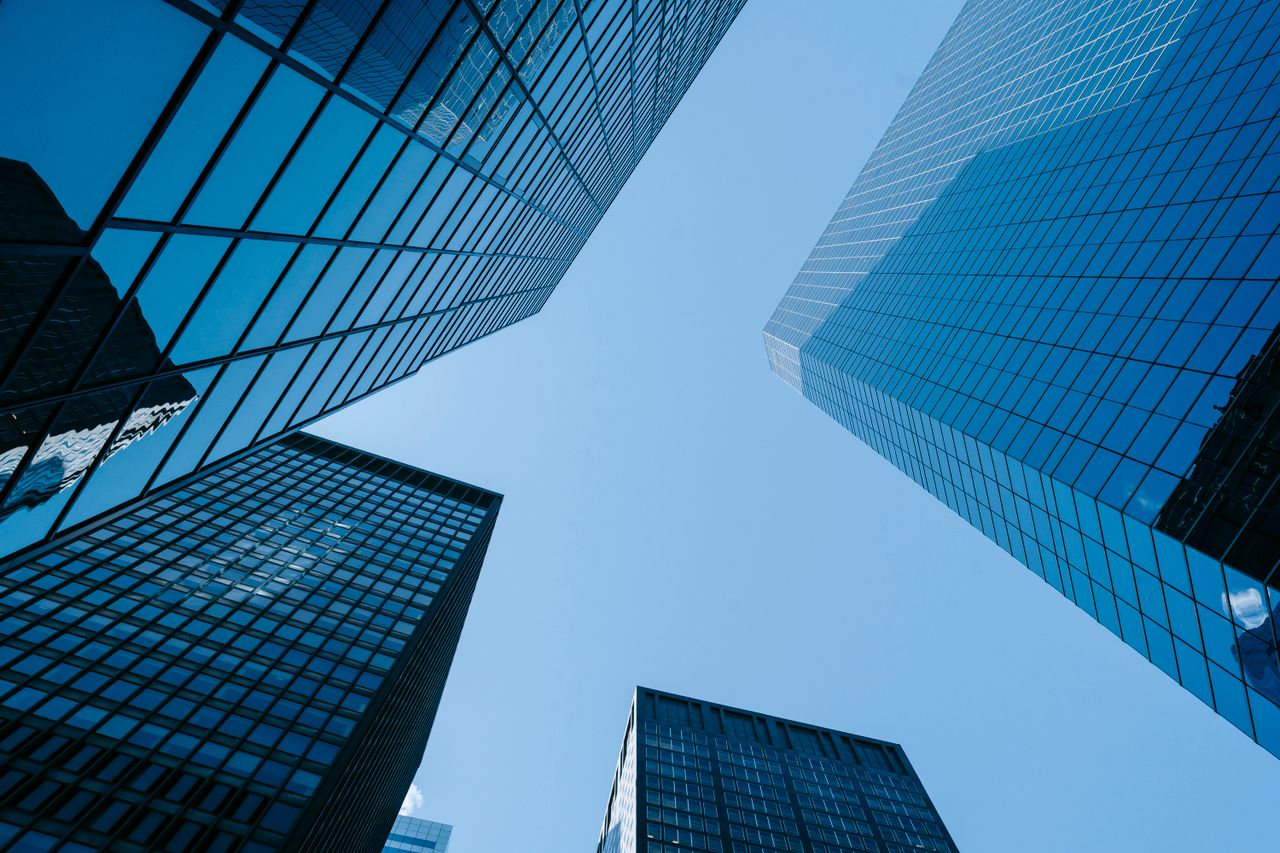 From below of contemporary high rise buildings with glass walls located on street with sunlight in modern district of city