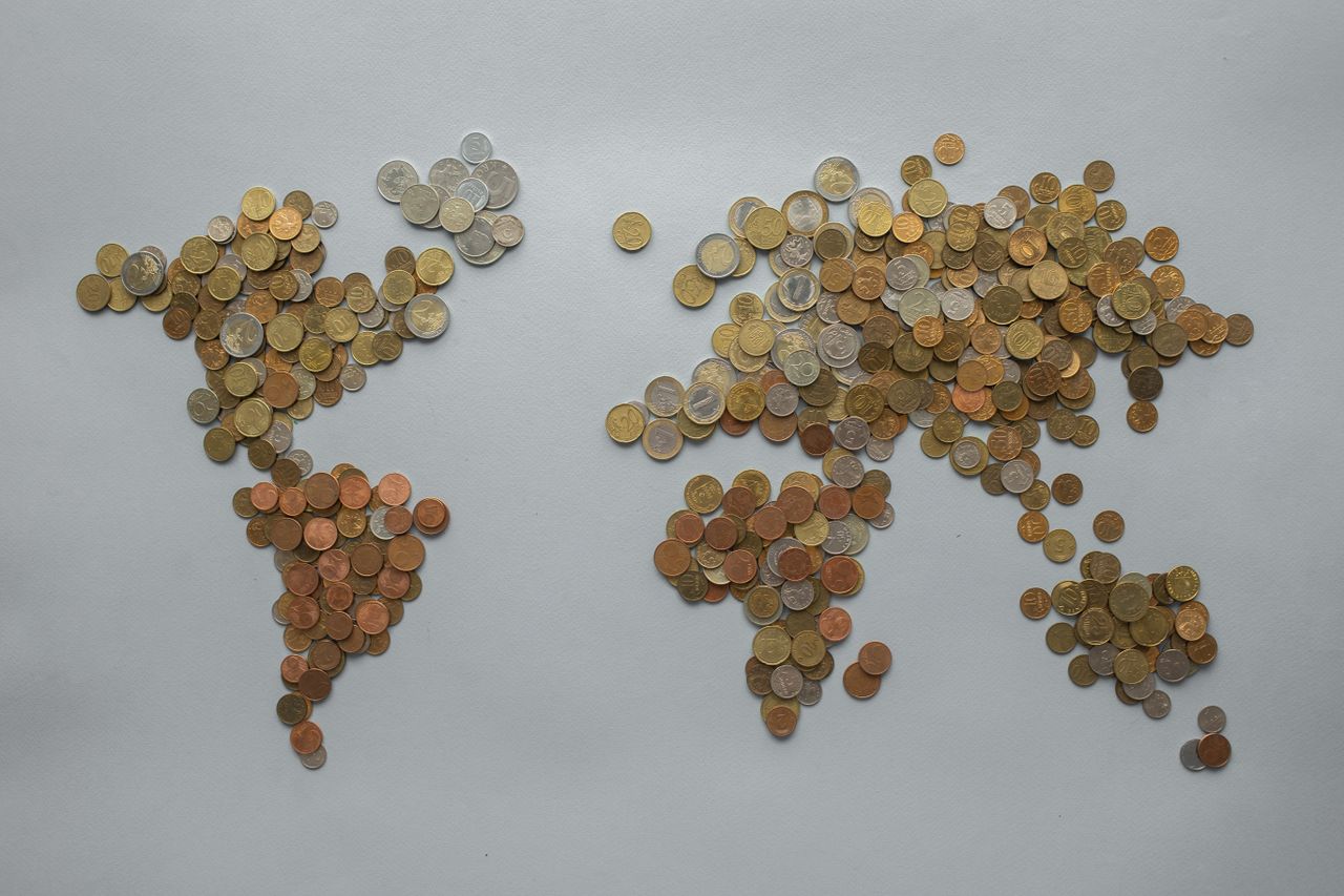 Creative world map made from assorted coins on a solid grey backdrop, symbolising global finance.