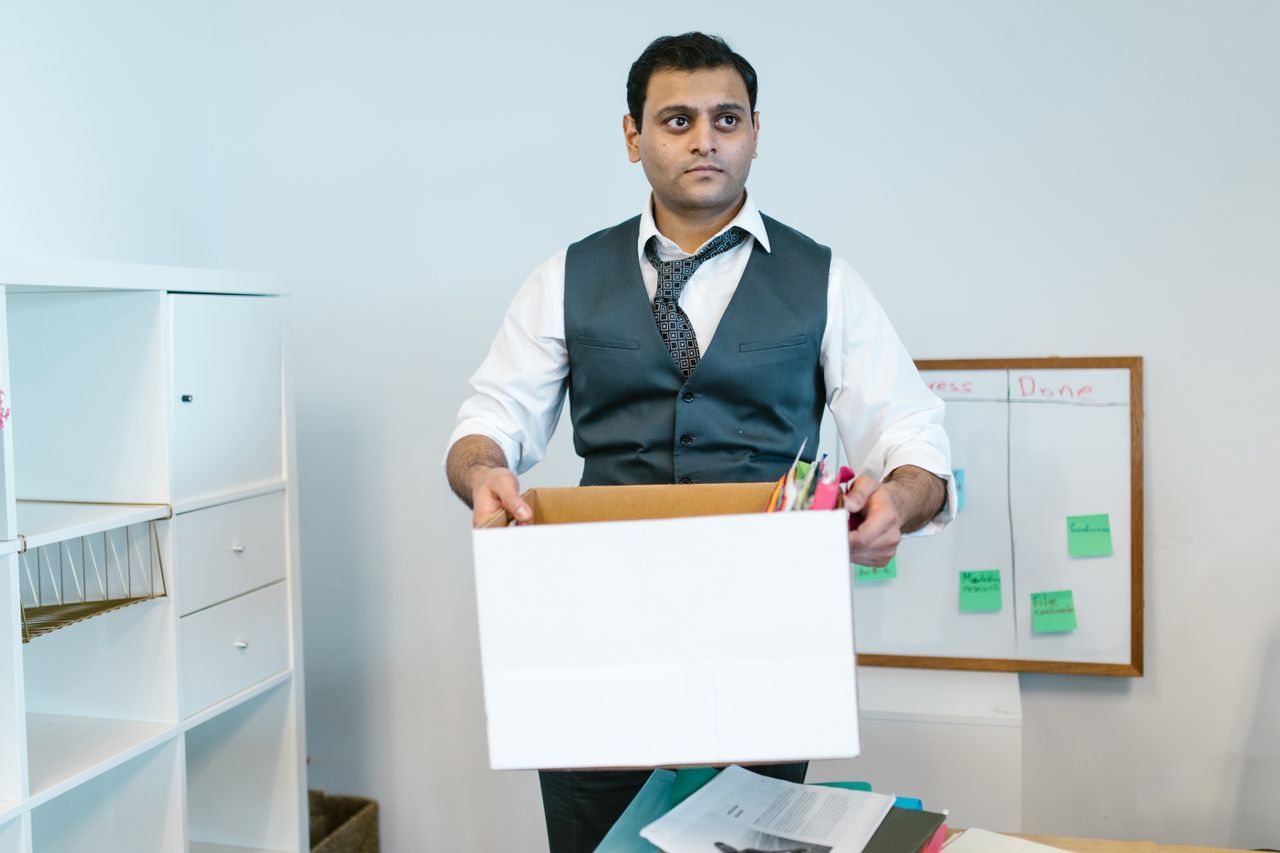 A man in a waistcoat holding a box of packed office items.