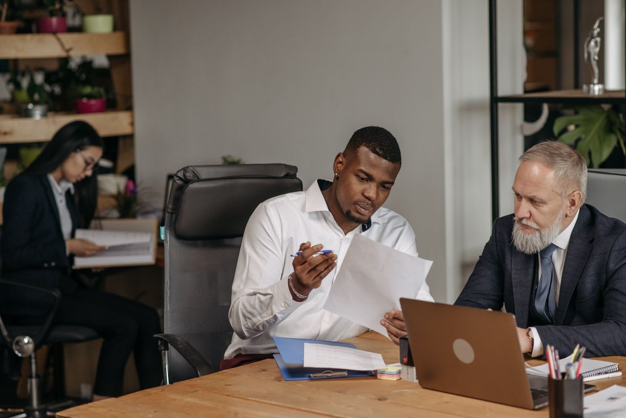 Three colleagues reviewing printed documents together in an office.