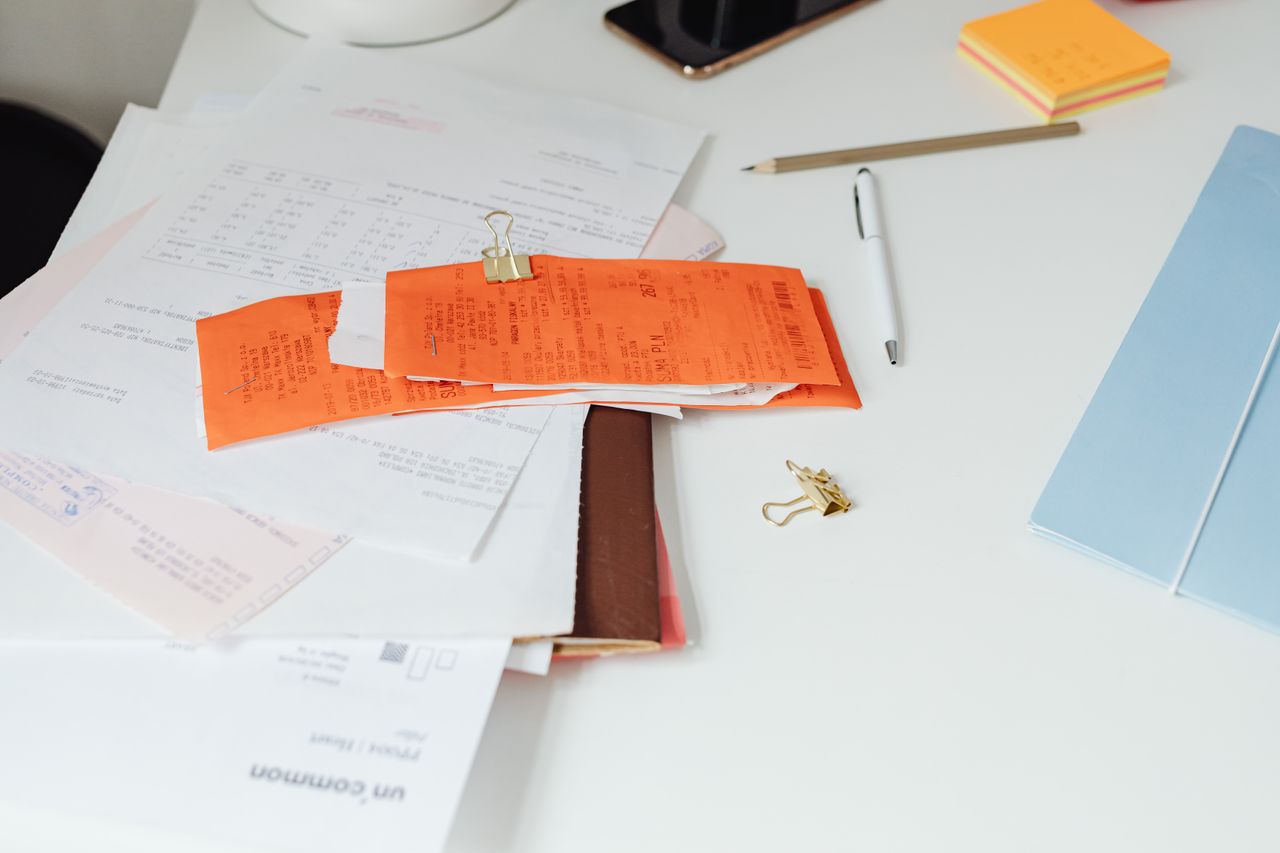 A desk with scattered receipts, documents and office stationery.