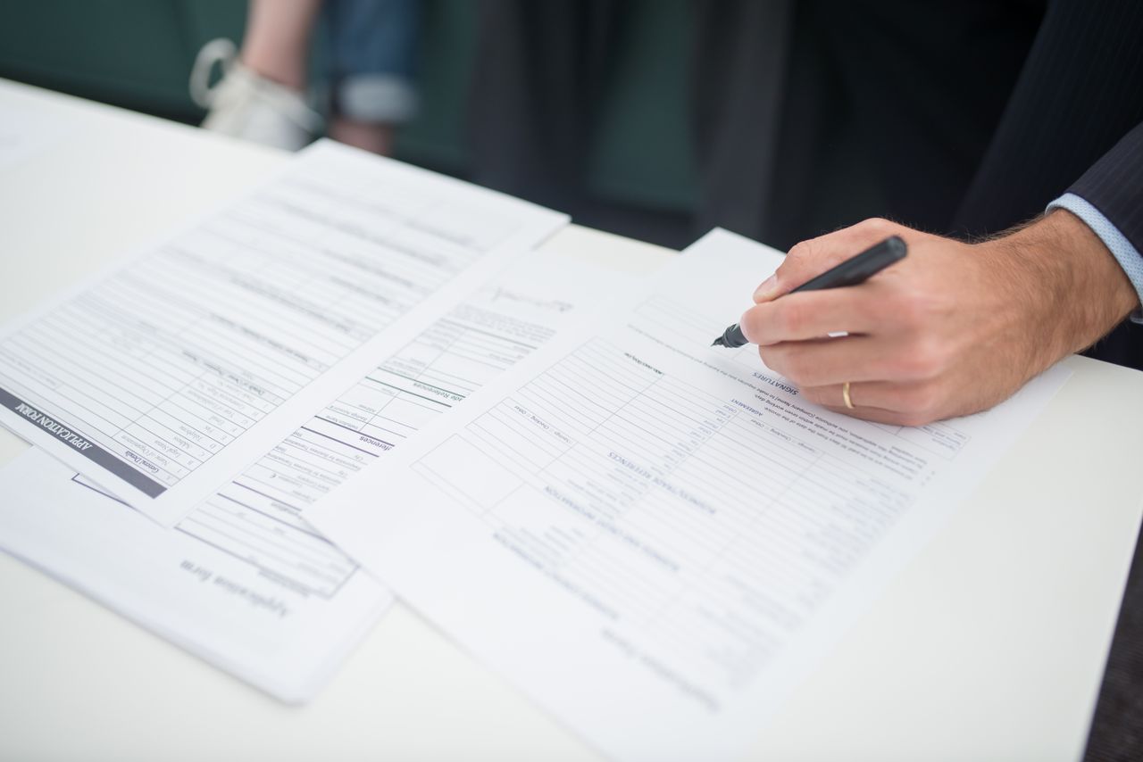 A hand signing a printed application form on a desk.