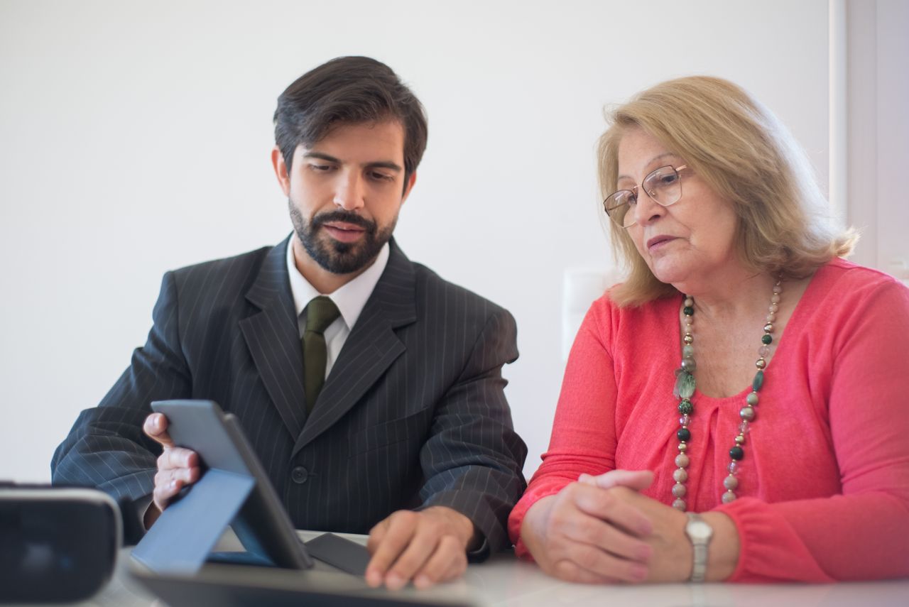 A younger man and an older woman talking over a tablet at a table.
