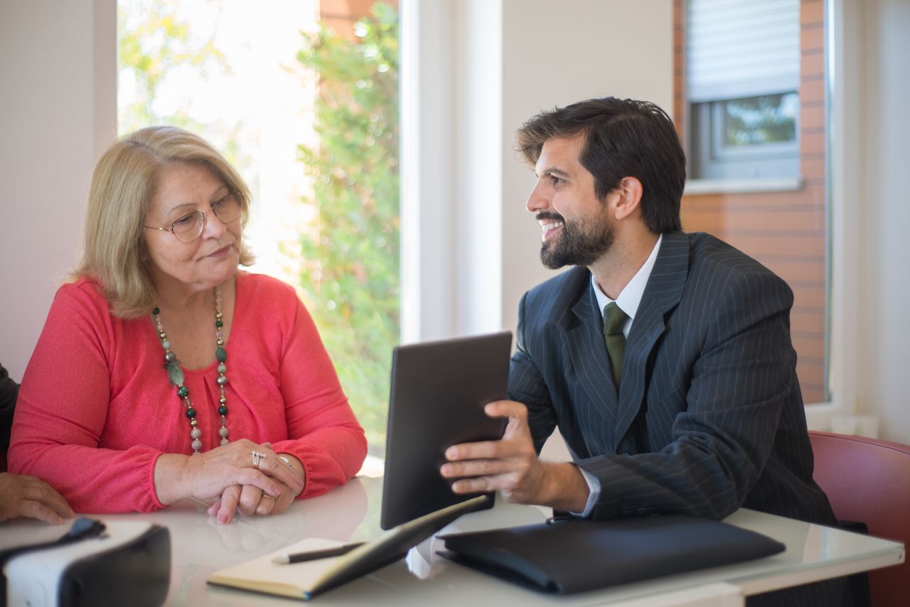 A younger man and an older woman reviewing details on a tablet.